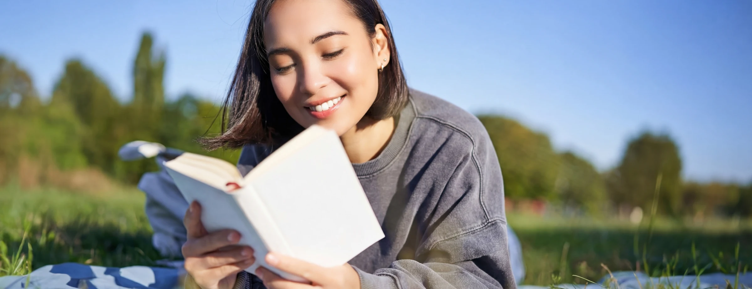 Mann liegt entspannt auf einer Decke auf einer grünen Wiese und liest ein Buch