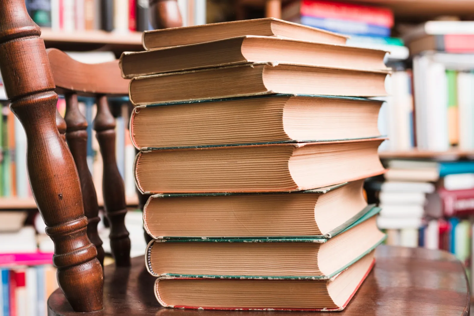 Stapel alter, gebundener Bücher auf einem Holzstuhl vor einem Bücherregal