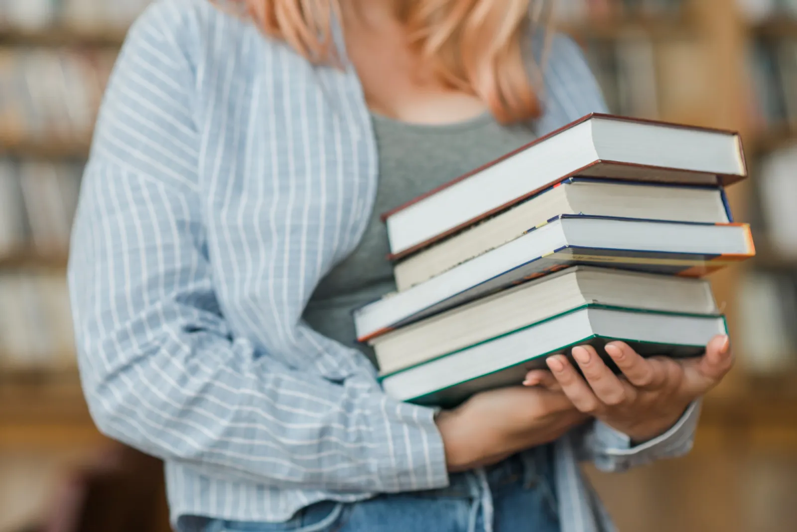 Person hält einen Stapel Fachbücher vor einem Bücherregal