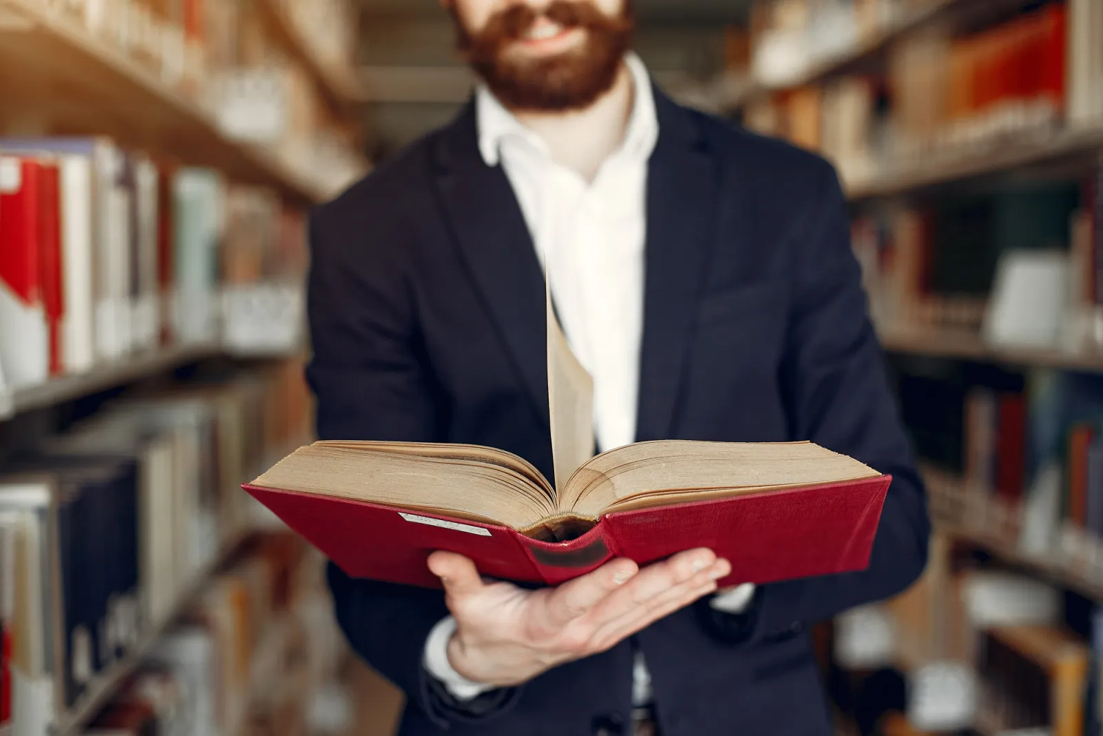 Mann im Anzug hält ein aufgeschlagenes Buch in einer Bibliothek
