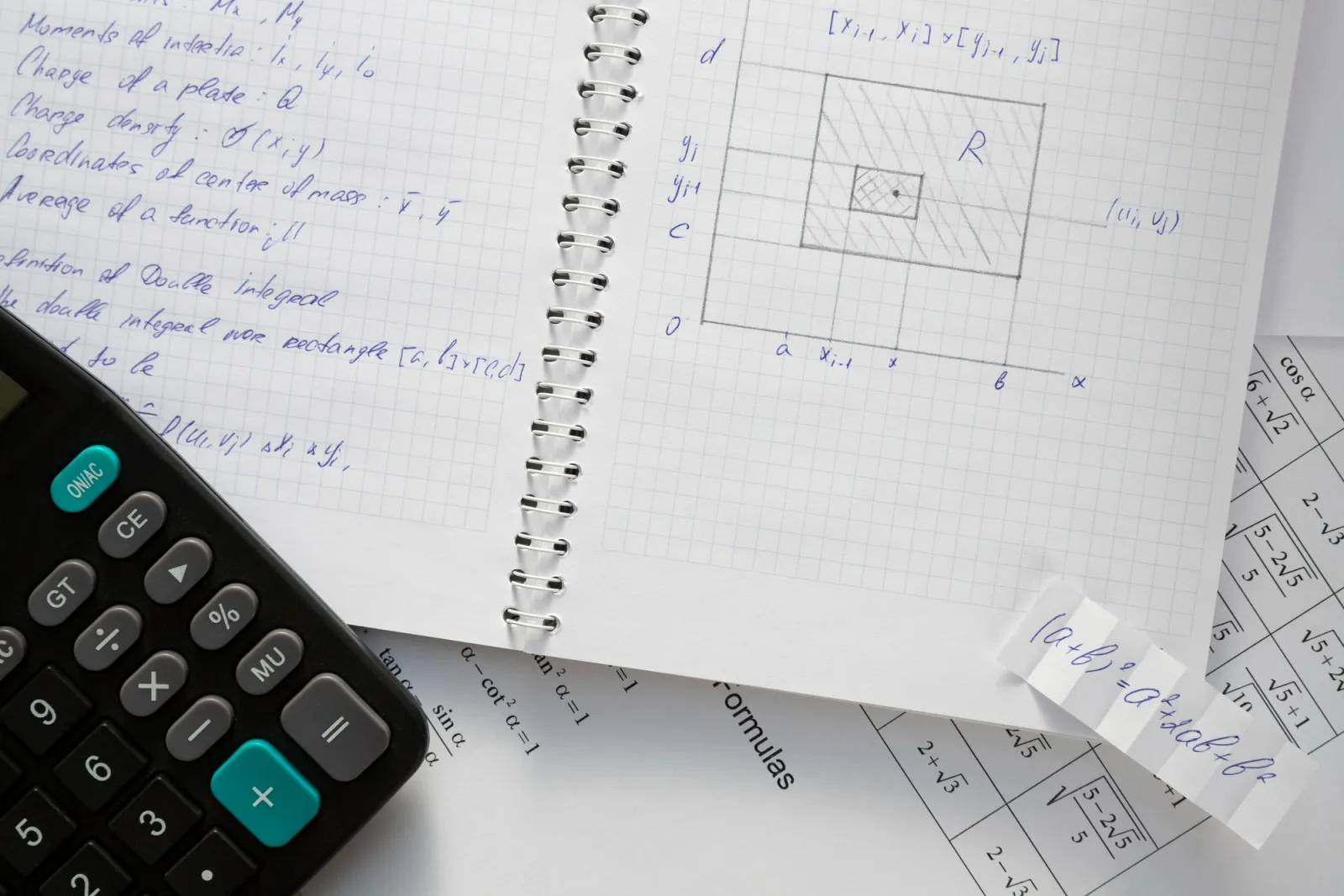 Handschriftliche mathematische Formeln in einem Notizblock neben Taschenrechner und Formelsammlung