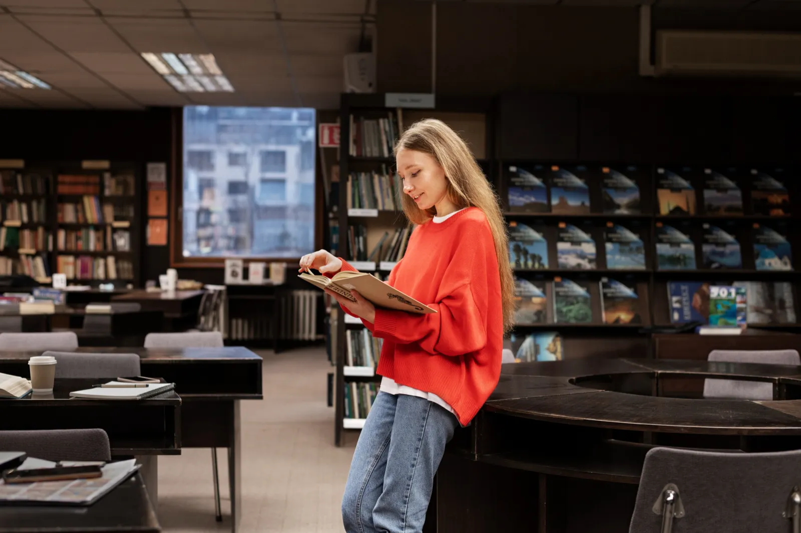 Junge Frau liest stehend ein Buch in einer Bibliothek